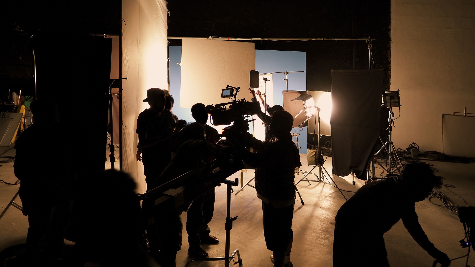 Silhouette of film crews and video camera on special dolly crane with film lights equipment and blue screen set. Film Production behind the scenes studio set in silhouette style. Behind video shooting